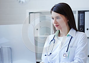 Female medicine doctor sitting at the table and looking at desktop computer screen.