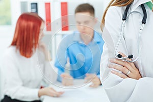 Female medicine doctors`s hands crossed on her chest closeup with family couple on the background