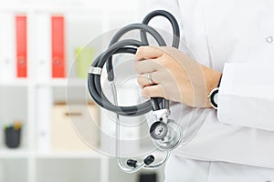 Female medicine doctors`s hands crossed on her chest holding stethoscope closeup.