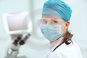 Female microbiologist in a protective mask looking at you.