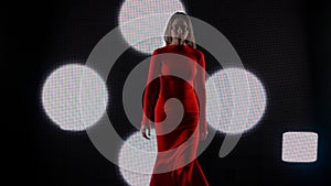 Female model against digital wall. Woman in red dress walking on runaway catwalk fashion show in front of digital screen