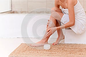 Female model applies moisturizer on her legs, enjoys perfectly smooth silky skin after epilation or home depilation