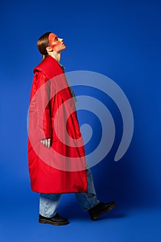 Female model in baggy coat walking against blue background