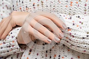 Female model hands with beige nail design. Glossy beige nail polish manicure. Woman hands on wool colorfull sweater