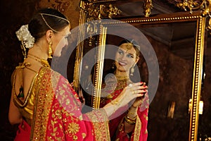 Female model Hindu Bride in saree, wearing gold and jasmine flower garlands in the hair near mirror, back view.