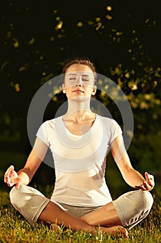 Female model meditating in serene harmony in lotus position in park.
