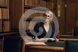 Female model sitting at desk and reading book at library