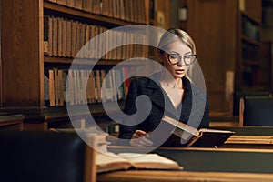 Female model sitting at desk and reading book at library