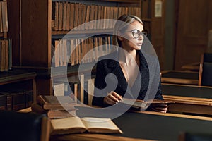 Female model sitting at desk and reading book at library