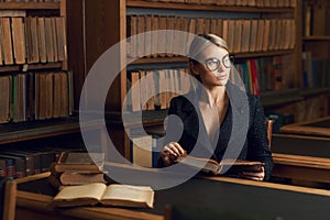 Female model sitting at desk and reading book at library