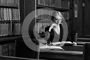 Female model sitting at desk and reading book at library