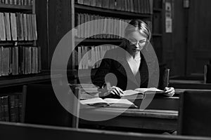 Female model sitting at desk and reading book at library