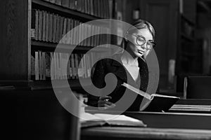 Female model sitting at desk and reading book at library