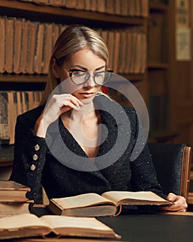 Female model sitting at desk and reading book at library