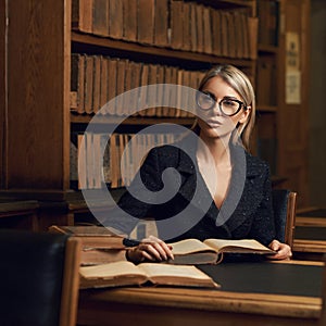 Female model sitting at desk and reading book at library