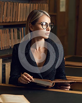 Female model sitting at desk and reading book at library