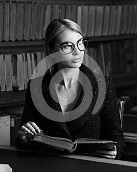 Female model sitting at desk and reading book at library