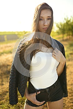 Female model standing on the field lit by warm sun rays, her hair blowing in the wind.