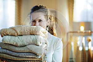 Female at modern home in sunny winter day holding sweaters