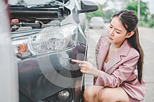 female motorist looks at the abrasion on the front of the car caused by a car accident while waiting for the insurance agent