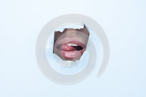 Female mouth with tongue out of a hole of blue paper background