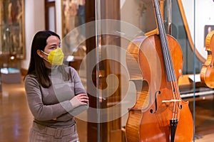 Female museum visitor in mask examining ancient musical instruments