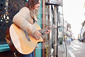 Female Musician Busking Playing Acoustic Guitar Outdoors In Street