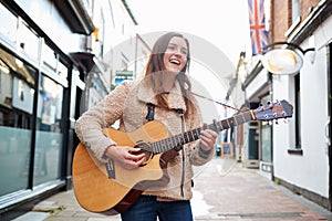 Female Musician Busking Playing Acoustic Guitar Outdoors In Street