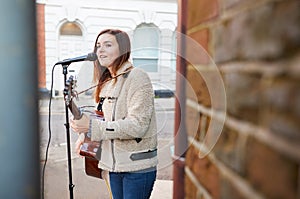 Female Musician Busking Playing Acoustic Guitar And Singing Outdoors In Street