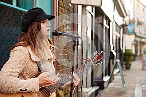 Female Musician Busking Playing Acoustic Guitar And Singing Outdoors In Street