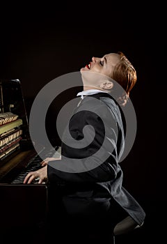 Female musician dressed in a man`s suit sitting next to the piano photo