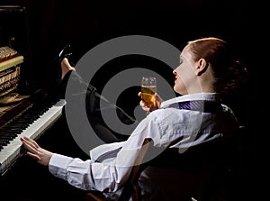 Female musician dressed in a man`s suit sitting next to the piano and drinks champagne photo