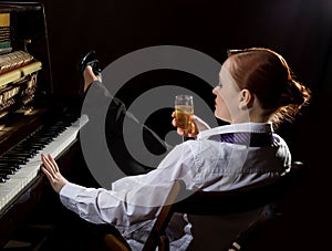 Female musician dressed in a man`s suit sitting next to the piano and drinks champagne photo