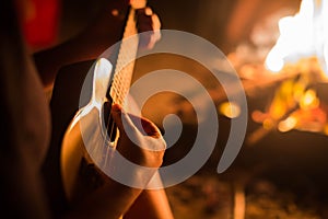 A female musician playing guitar outside, sitting next to a fire. Relaxation