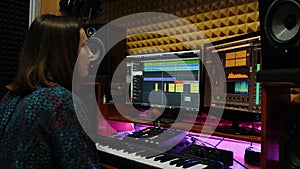 Female musician songwriter playing piano midi keyboard in recording studio. Woman sound engineer working at home music studio with