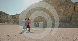 Female musicians in blowing dresses play the violins on nature at cliff