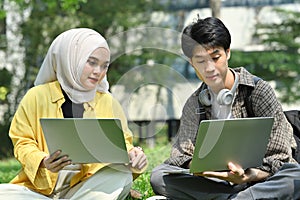 Female Muslim college student and classmates making research, working on group project on laptop at outdoor