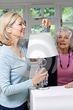 Female Neighbor Helping Senior Woman Change Lightbulb In Lamp