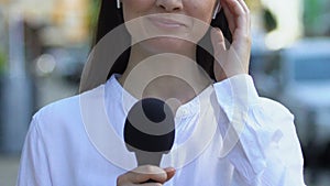 Female newscaster with microphone wireless earphones presenting news, reportage