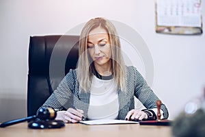 A female notary public sits at a wooden desk in her notary office signs documents.