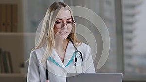 Female nurse caucasian woman medical assistant in glasses video calling distant patient on laptop. Doctor girl therapist