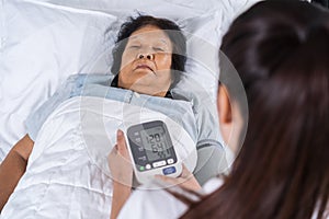 Female nurse checking blood pressure of a senior woman on bed