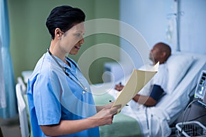 Female nurse checking patient report in ward