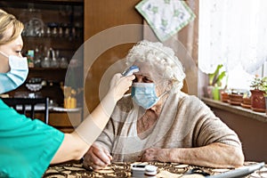 Female nurse checking temperature to senior woman during home visit