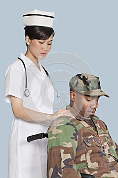 Female nurse comforting disabled US Marine Corps soldier in wheelchair over light blue background