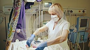 Female nurse doctor taking care of newborn baby inside incubator. Woman nurse looking at newborn baby sleeping inside