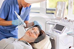 Female nurse doing cosmetology procedure for elderly woman, RF lifting and deep hydration for facial skin therapy