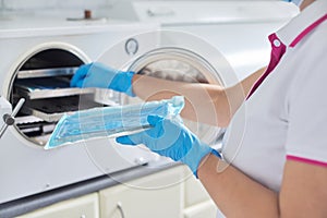 Female nurse doing sterilization of dental medical instruments in autoclave