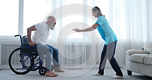 Female nurse encouraging disabled old patient to get out of the wheelchair