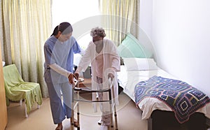 Female nurse helping senior female patient to stand with walker